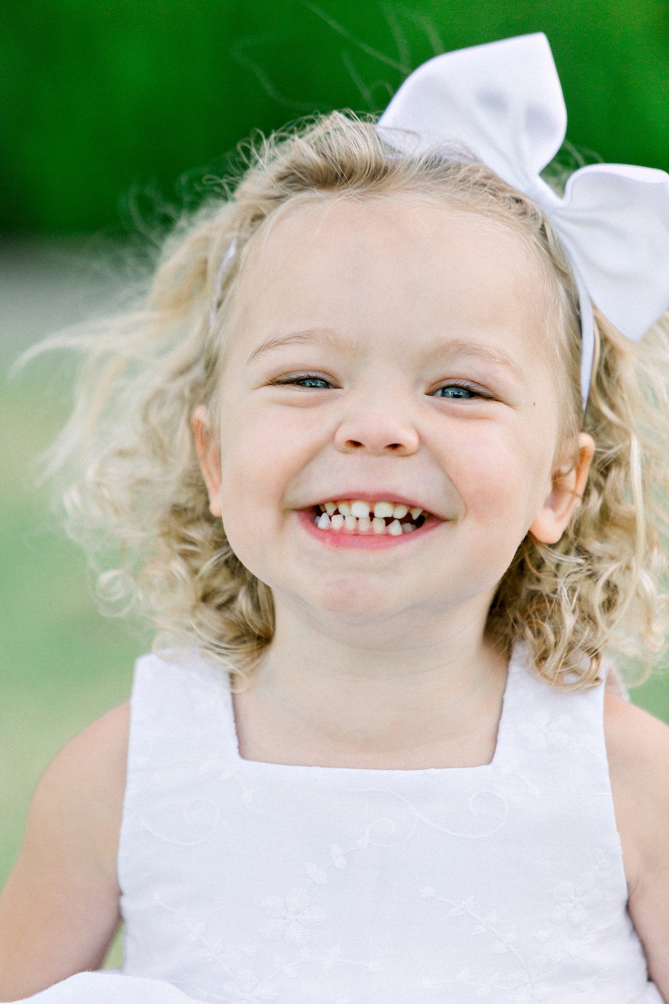 A girl smiling with a white bow.