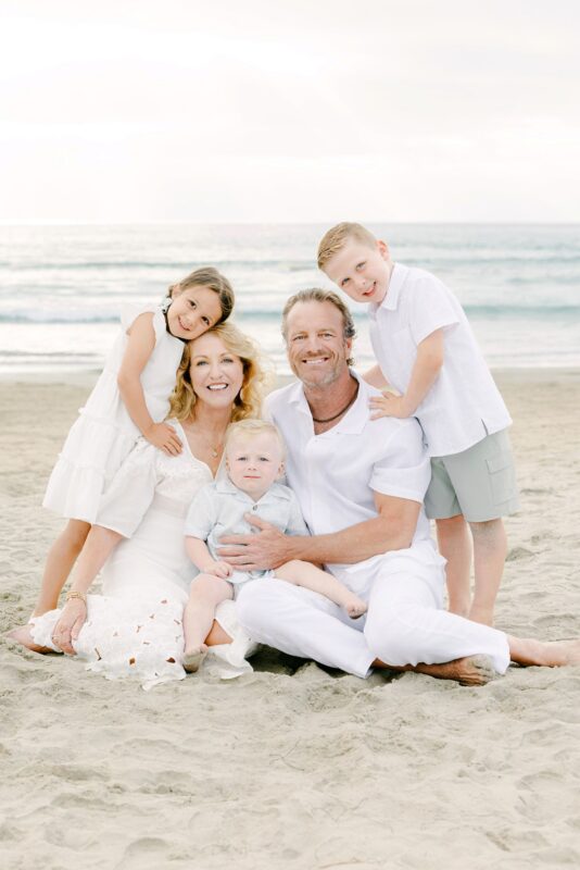 A family of five smiles on a sandy beach, captured beautifully by family photographers in Carlsbad.
