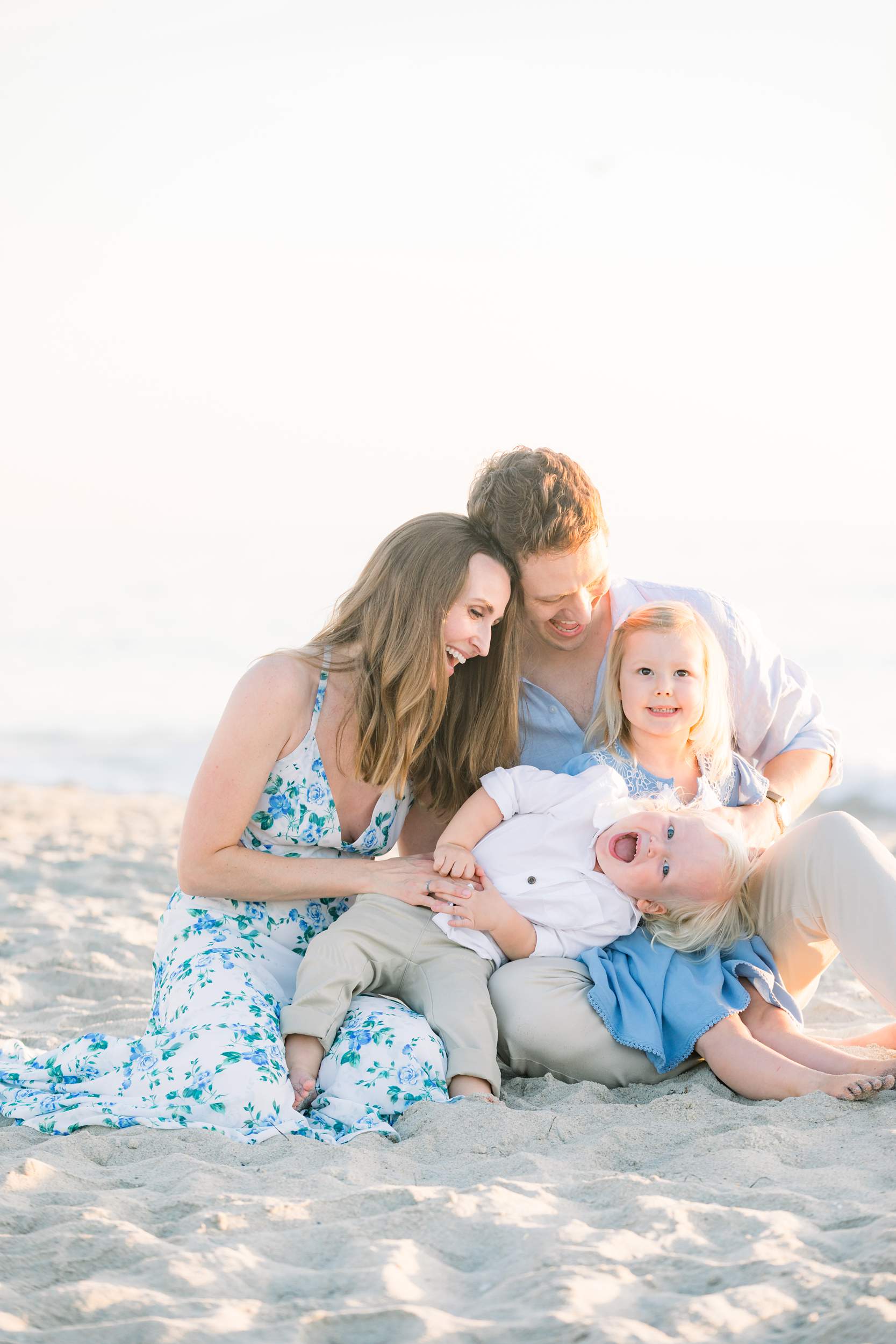 A happy family of four sits on Carlsbad Beach, smiling and laughing together—perfect for family portraits on a sunny day.