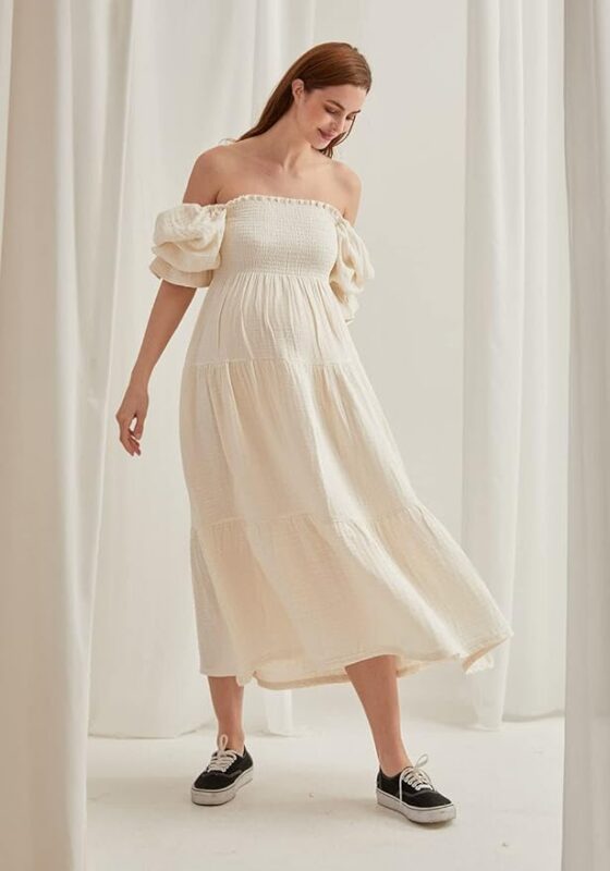 Woman in an off-shoulder, cream-colored maxi dress—perfect for portrait session dresses—smiling in black sneakers.