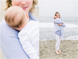 A woman in light clothing holds a baby wrapped in a blanket on a sandy beach by the ocean. Carlsbad Newborn Photographer.