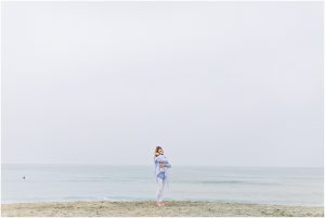 A woman holding a baby on a beach, captured by a Carlsbad Newborn Photographer.