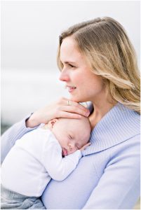 Carlsbad Newborn Photographer captures a woman in a light purple sweater cradling her sleeping baby close.