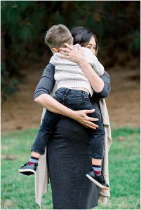 A woman hugs a young boy tightly during a heartfelt Solana Beach pregnancy photos maternity session outdoors.