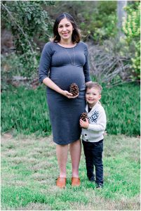 A pregnant woman and a young boy hold pinecones and smile during a joyful Solana Beach maternity session.