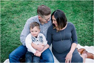 A family smiles together on a blanket in the grass during their Solana Beach pregnancy photos.