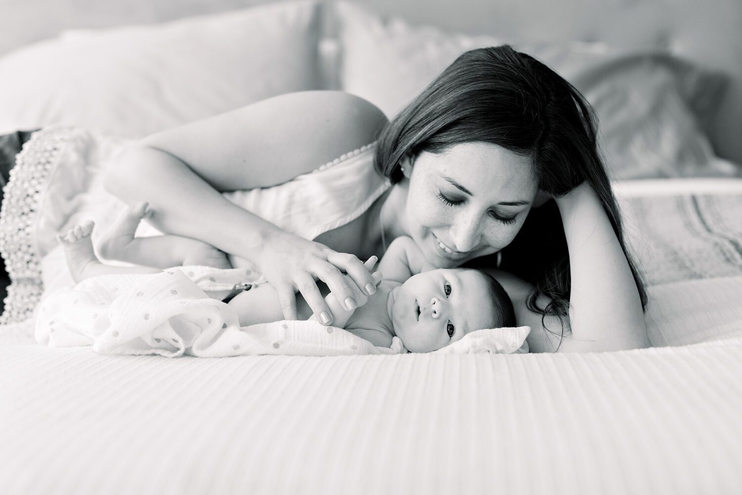 New mother and newborn baby cuddling skin to skin contact on a bed in home newborn photography session