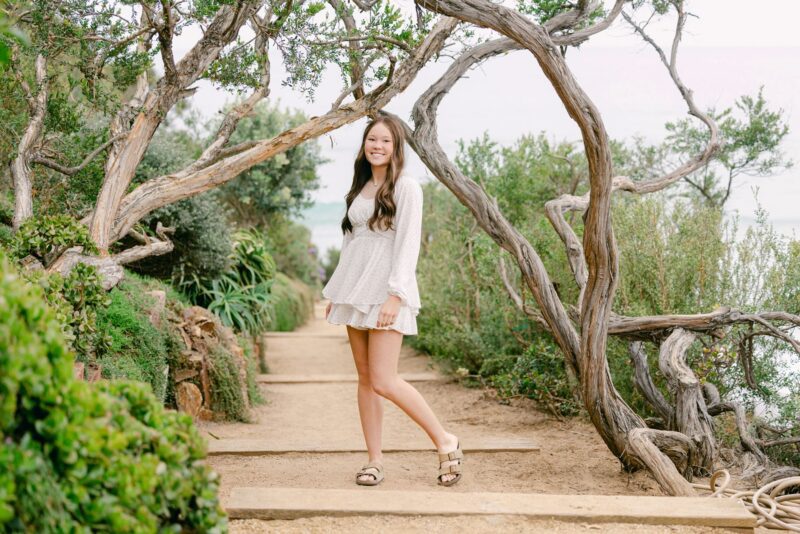High school, senior girl in a white dress stands on a dirt path—perfect inspiration for senior portraits ideas.