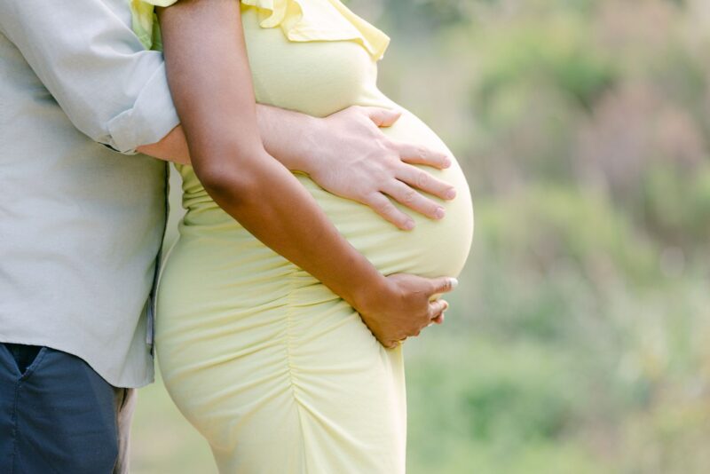 A couple gently holding a pregnant belly outdoors, captured by a Carlsbad Maternity Photographer.