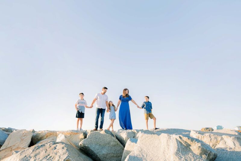 Five people, including three children, stand on large rocks under a clear sky, holding hands and smiling.