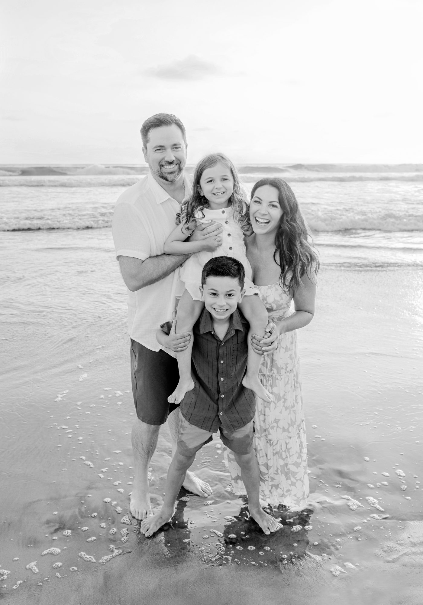 Family of four standing in the shallow surf at the beach, black and white