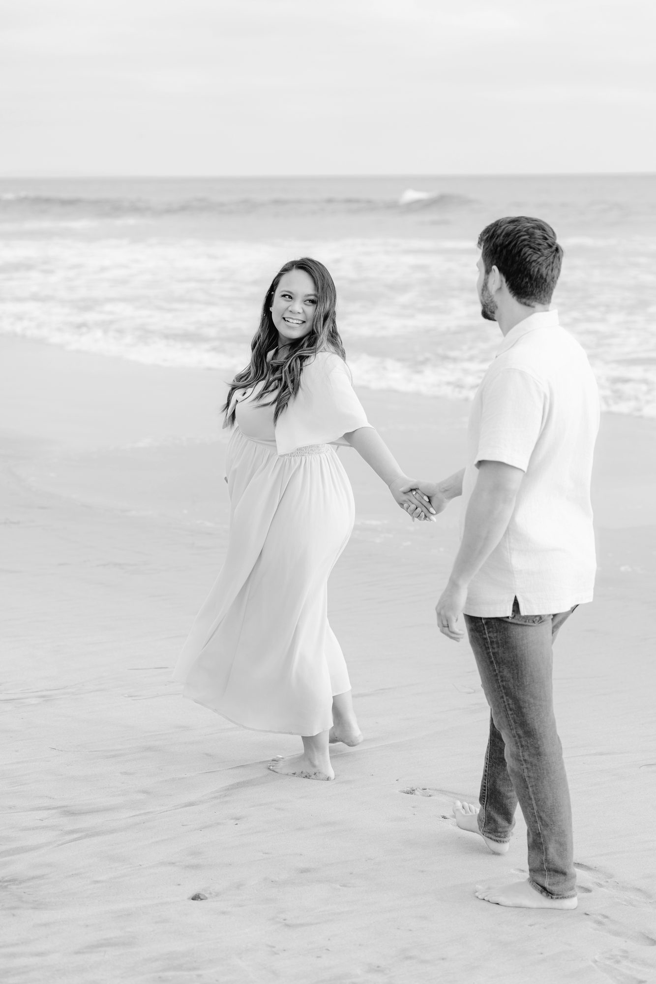 Expectant couple walking hand in hand along the shore, black and white