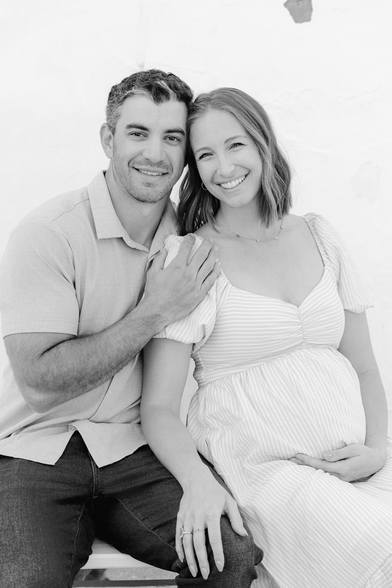 Expectant couple seated together in the Carlsbad studio, black and white