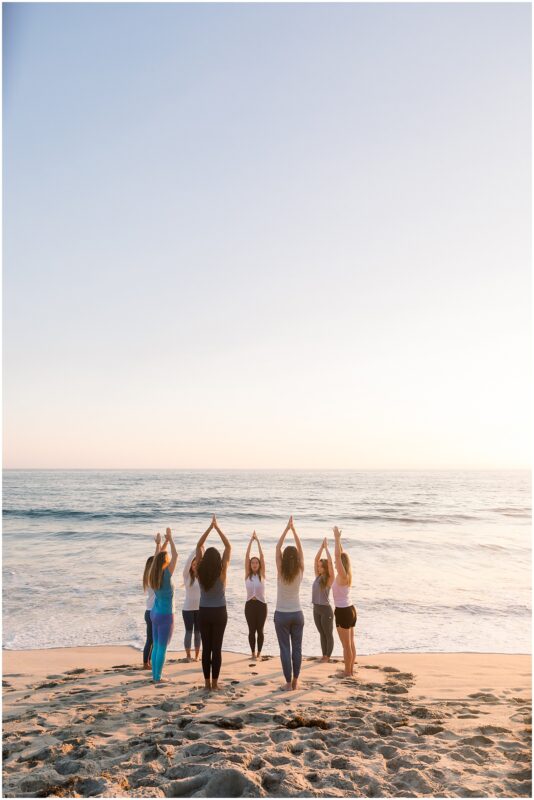 Yoga class practicing yoga on the beach at sunset