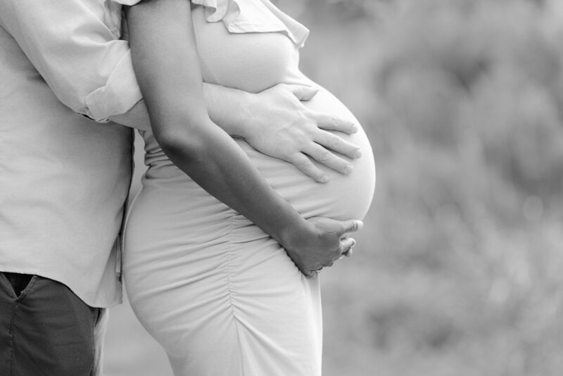 A couple gently holds the womans pregnant belly outdoors, showing love and anticipation for their baby.