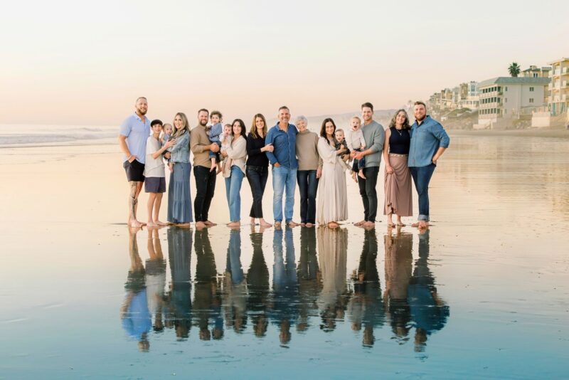 A large family stands barefoot on a beach at sunset, smiling together—captured by a San Diego Family Photographer.