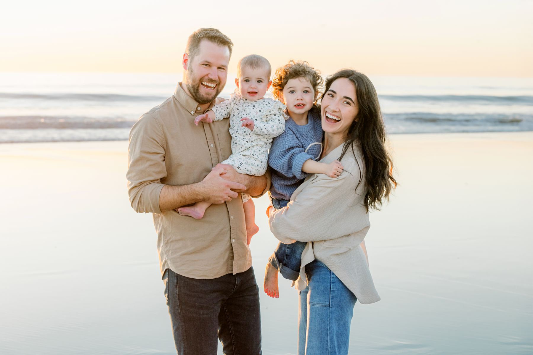 Family of four smiling and standing together on a beach at sunset—captured by a San Diego Family Photographer.