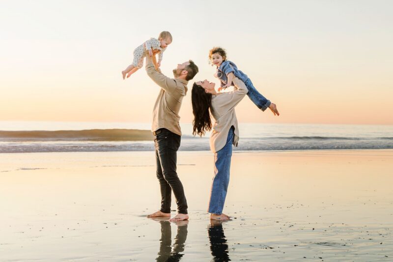 Two adults and two children play on a beach at sunset, captured by a San Diego Family Photographer.