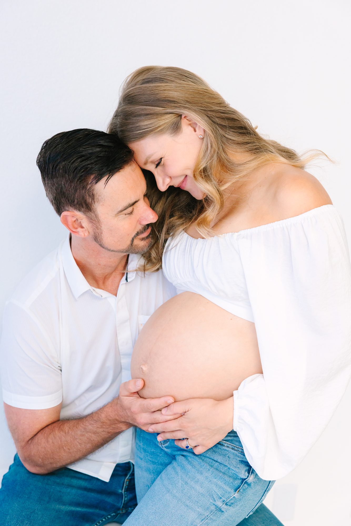 Expectant parents with their foreheads together and hands on her belly