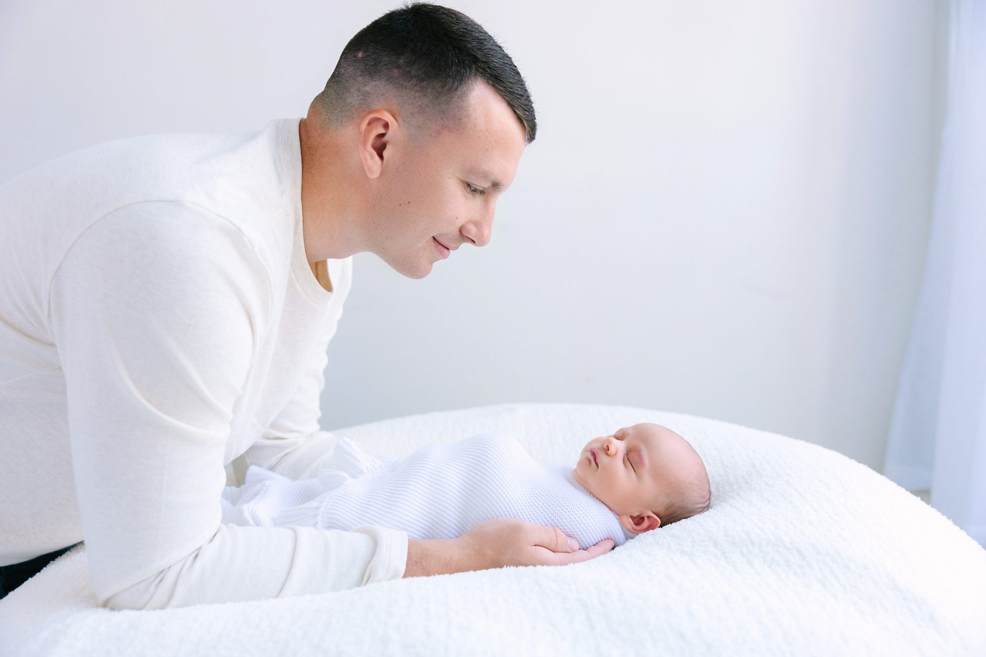 Father leaning over his newborn baby on a white bed
