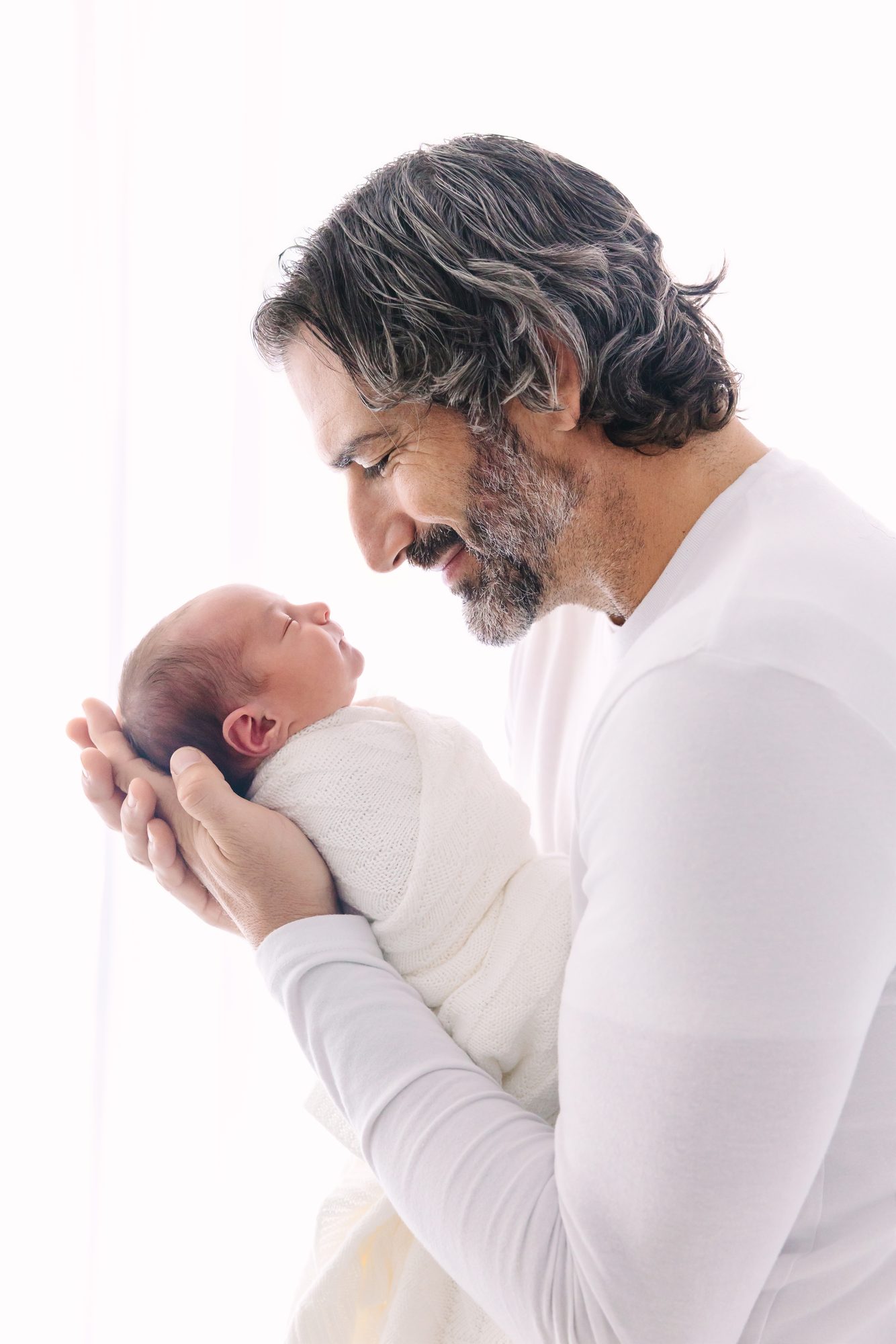 Father cradling his newborn in his hands by the window