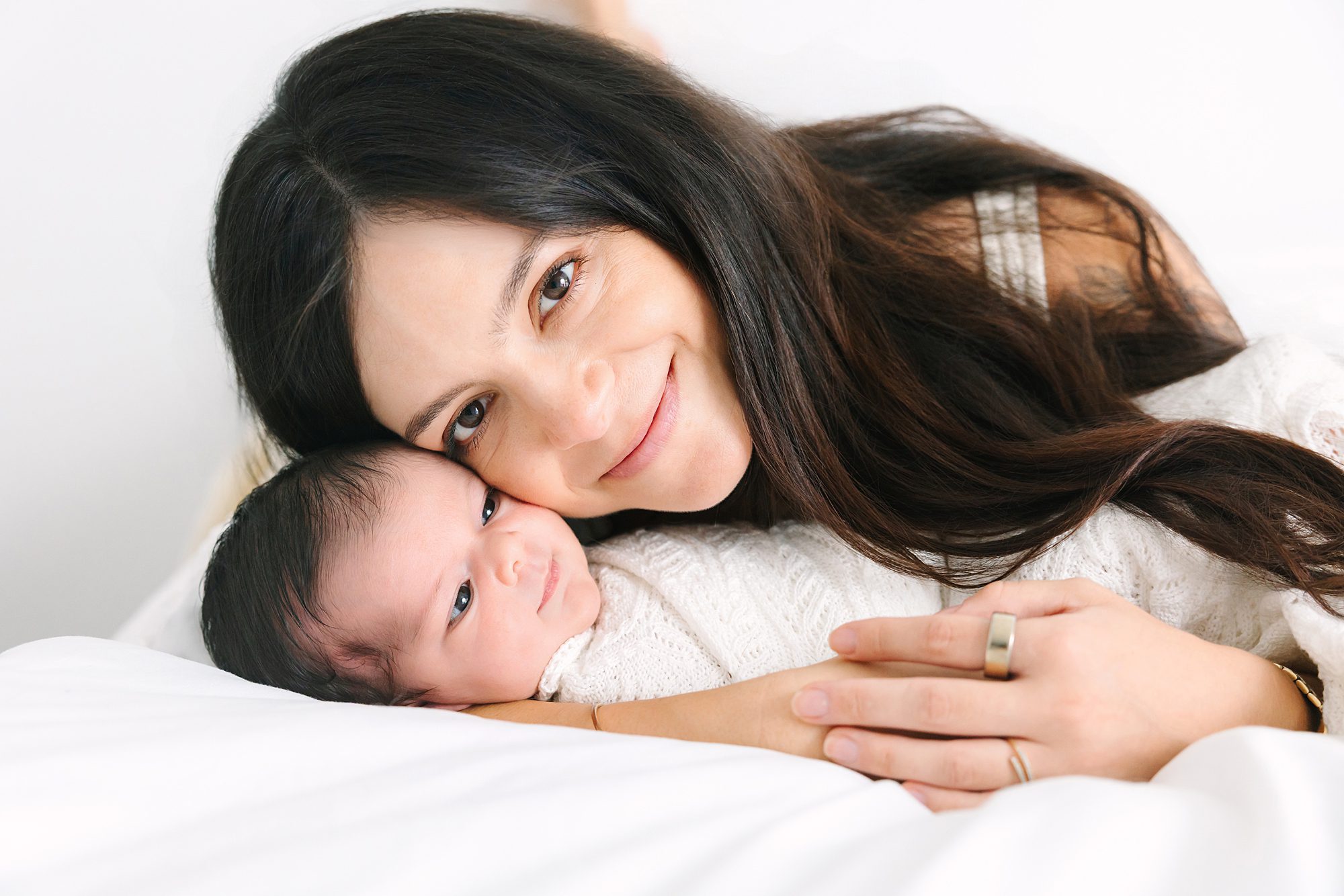 A mother cradling her newborn baby while lying on white bedding.