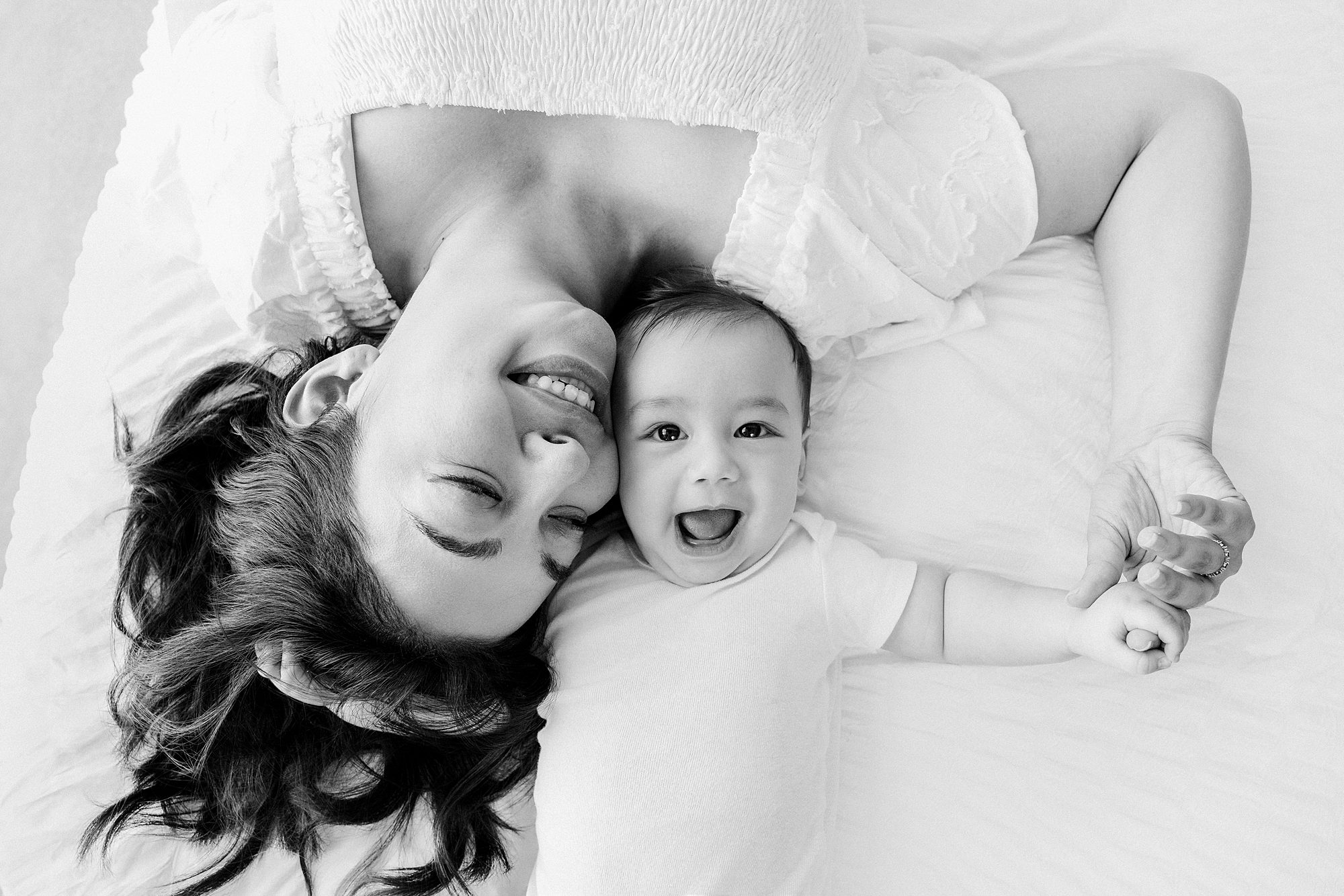 A mother lying on a bed with her laughing baby.