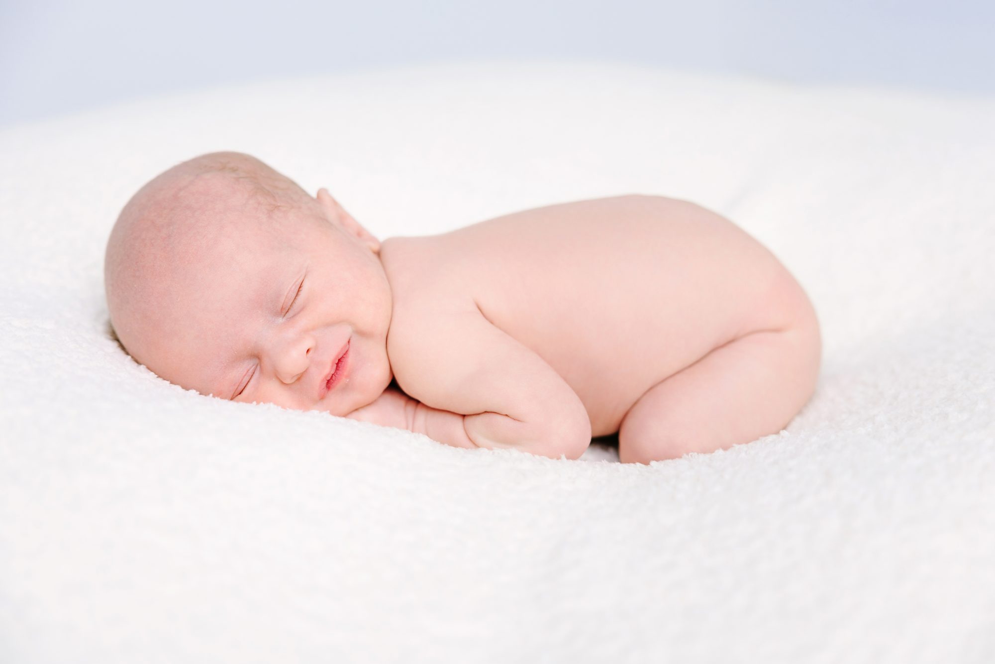 Newborn baby asleep on a soft white blanket in the Carlsbad studio