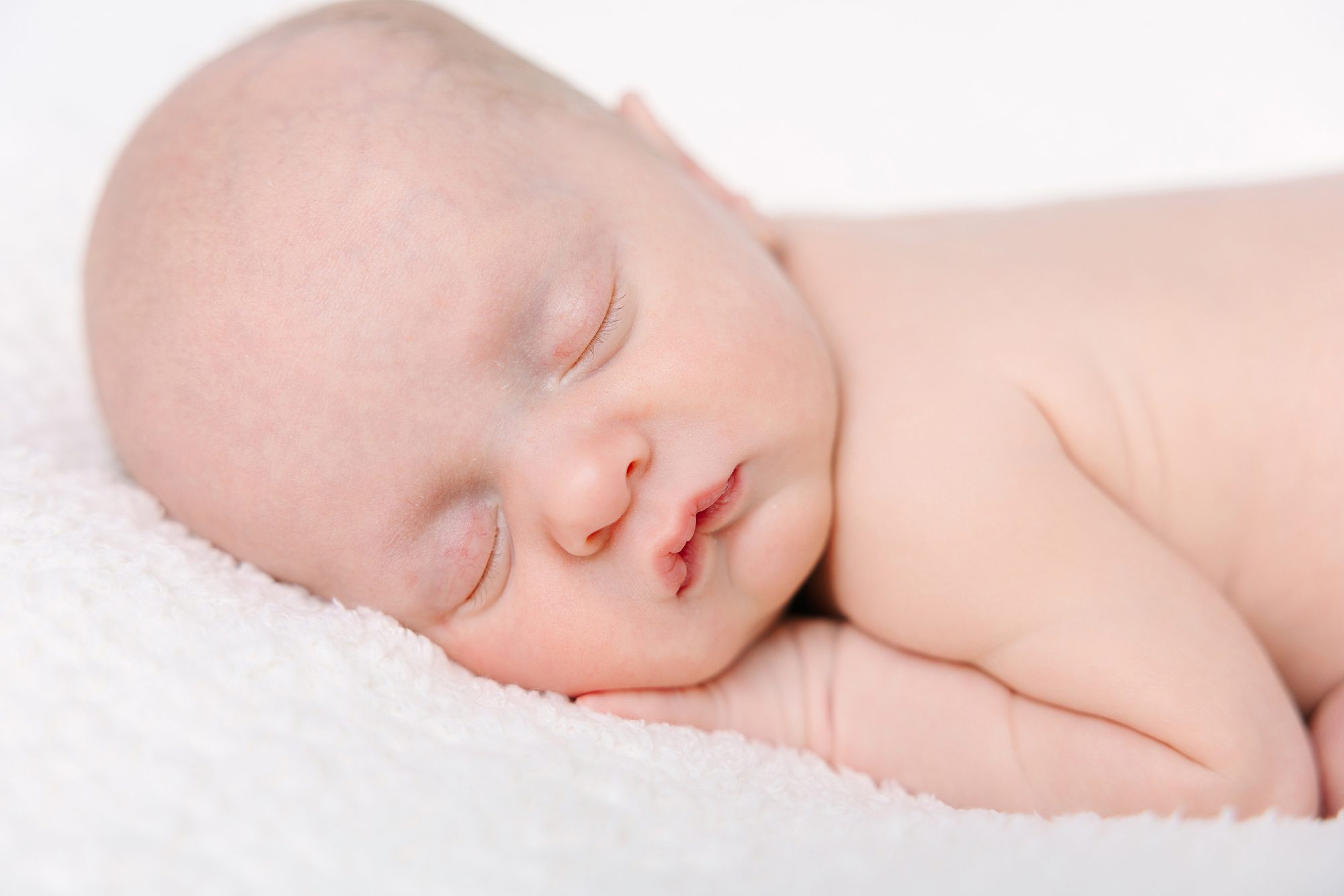 A newborn baby sleeping on a white textured blanket.