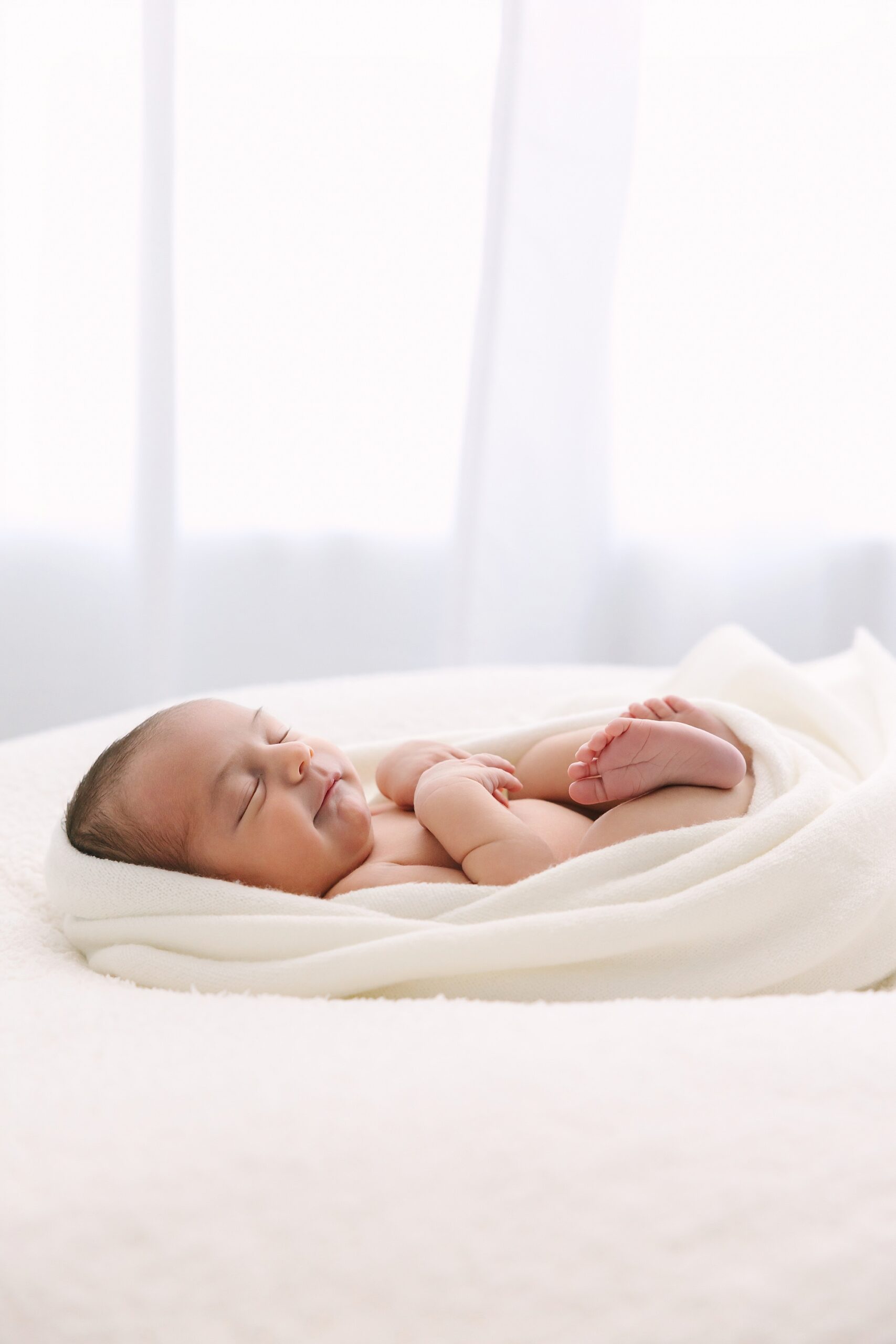 A newborn baby sleeping soundly, wrapped in a soft white blanket.