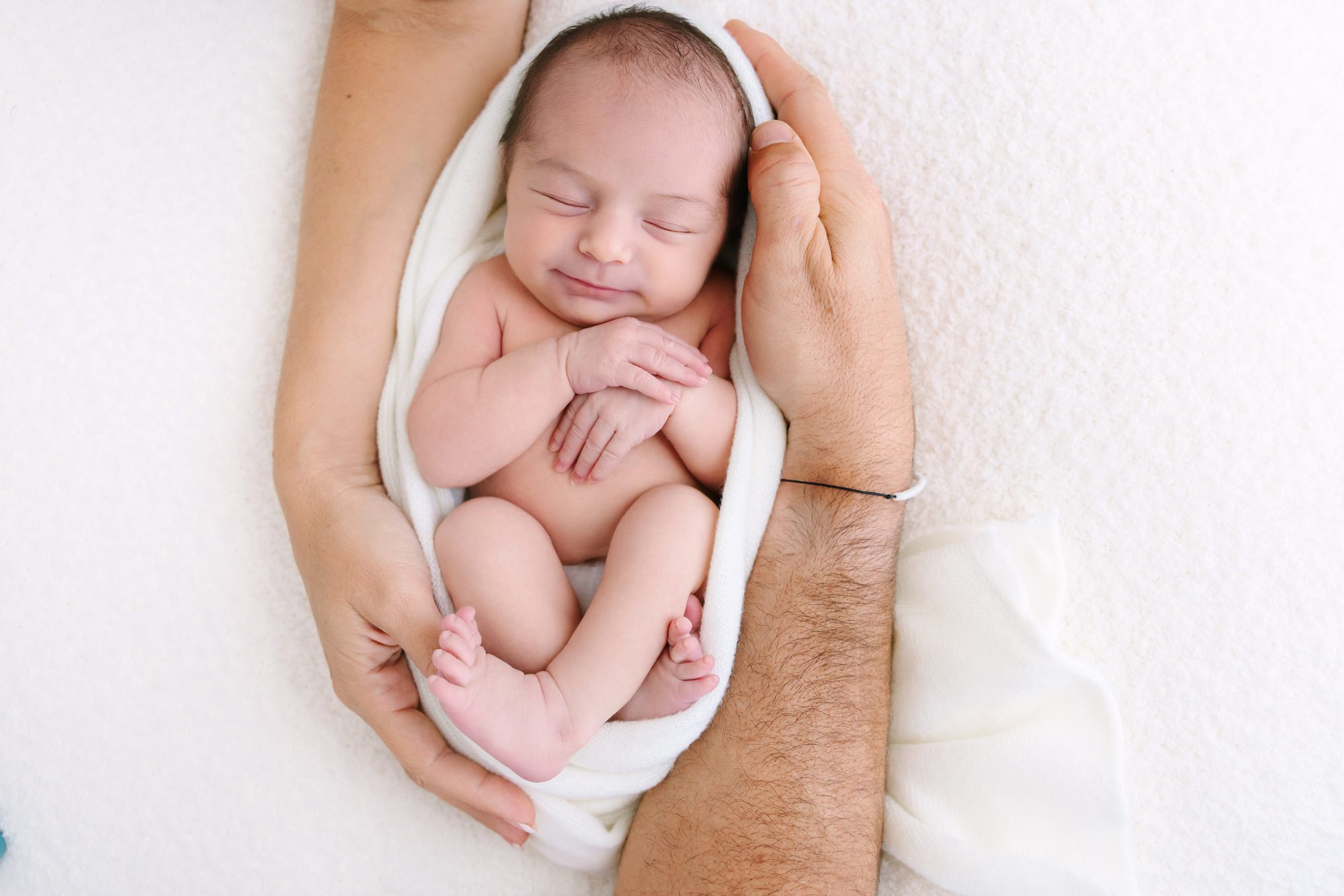Newborn baby curled up in dad's hands on a white blanket