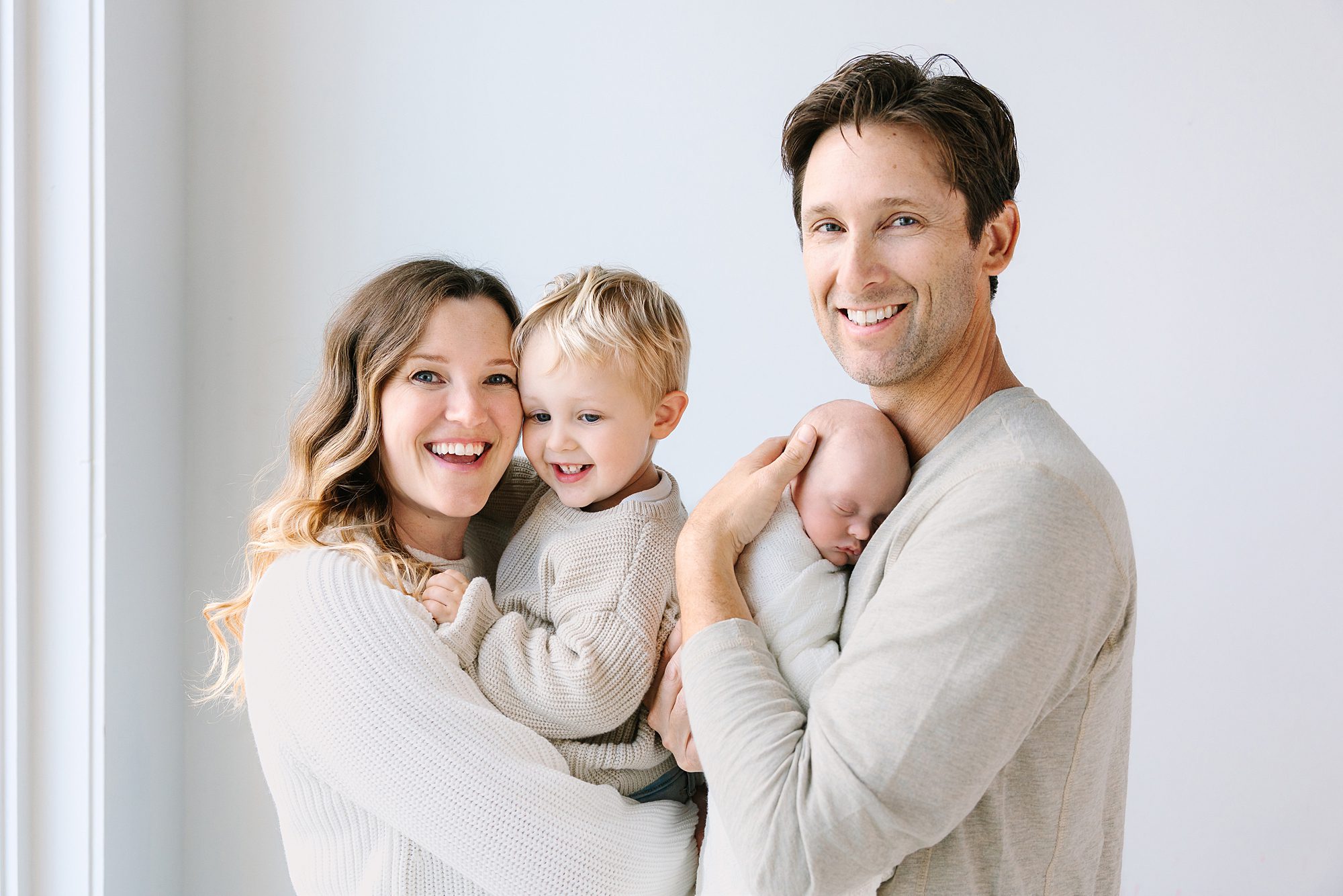 A smiling couple posing with their young son and newborn baby.