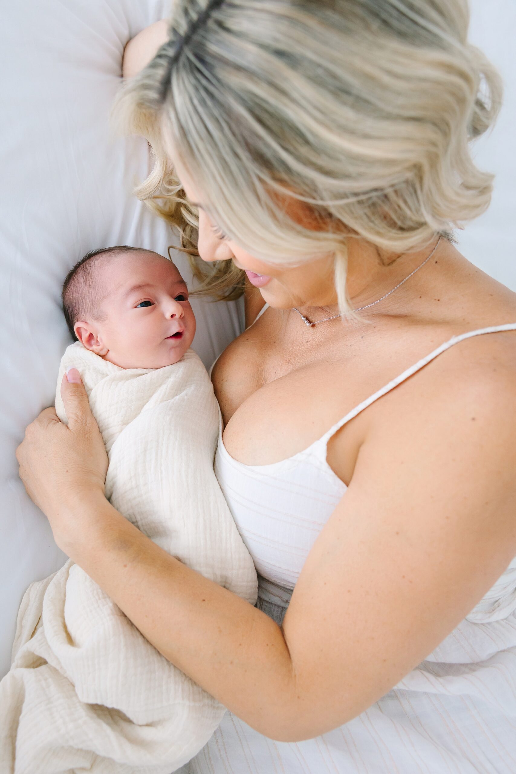 A woman smiles down at her newborn baby wrapped in a white swaddle.