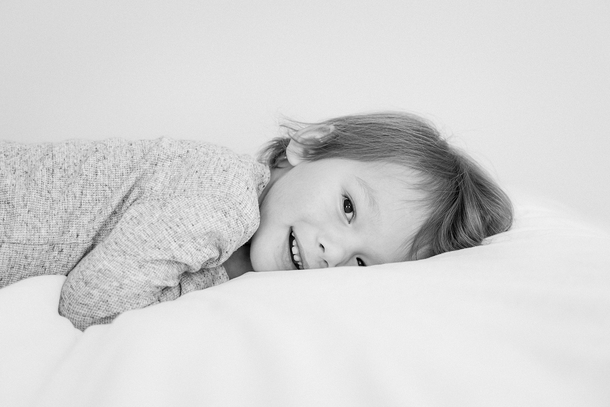 A young child lying on a pillow and smiling at the camera.