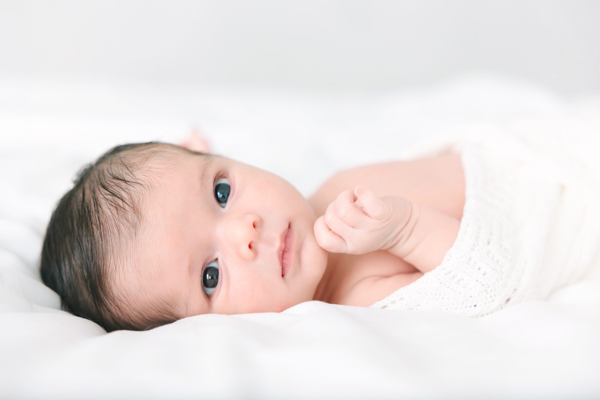 Wide-eyed newborn lying on a white bed