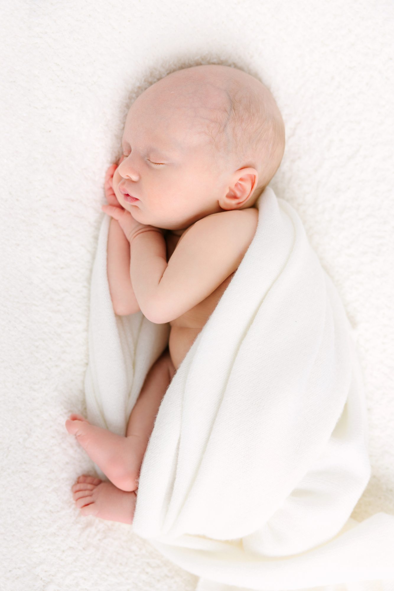 Sleeping newborn wrapped in a cream blanket, studio newborn portrait