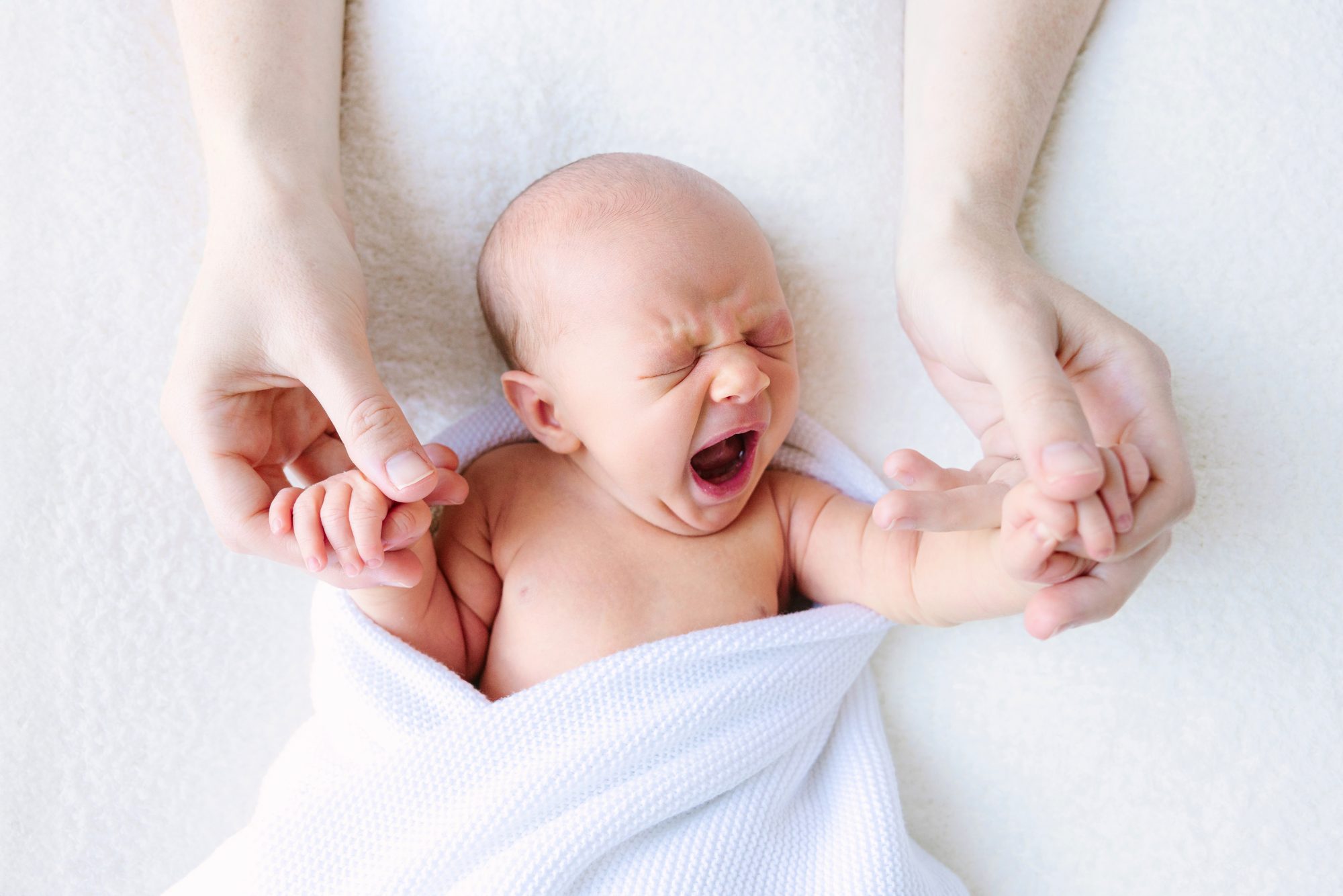 Yawning newborn held gently in a parent's hands