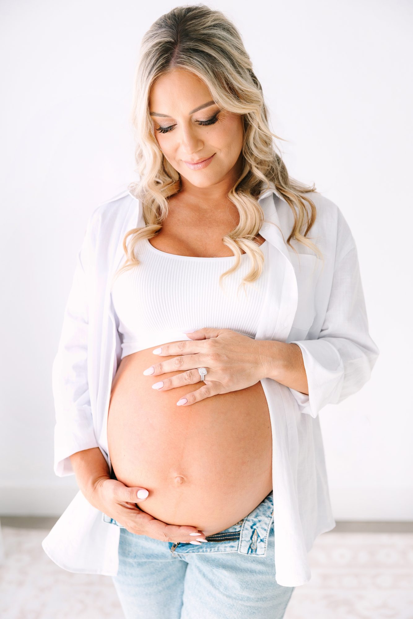 Expectant mother in an open white shirt cradling her belly, studio maternity portrait