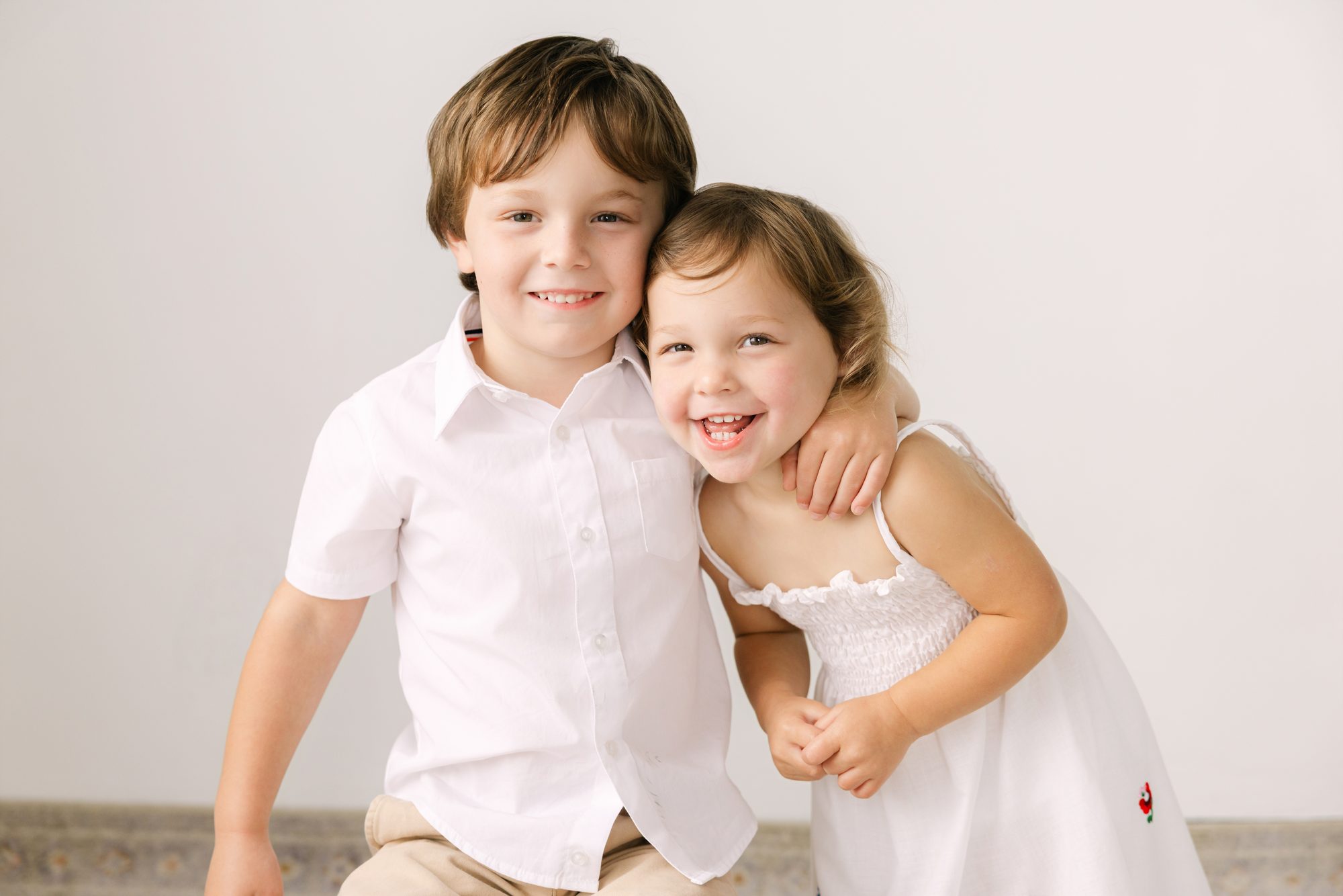 Brother and sister hugging and laughing during a studio family session