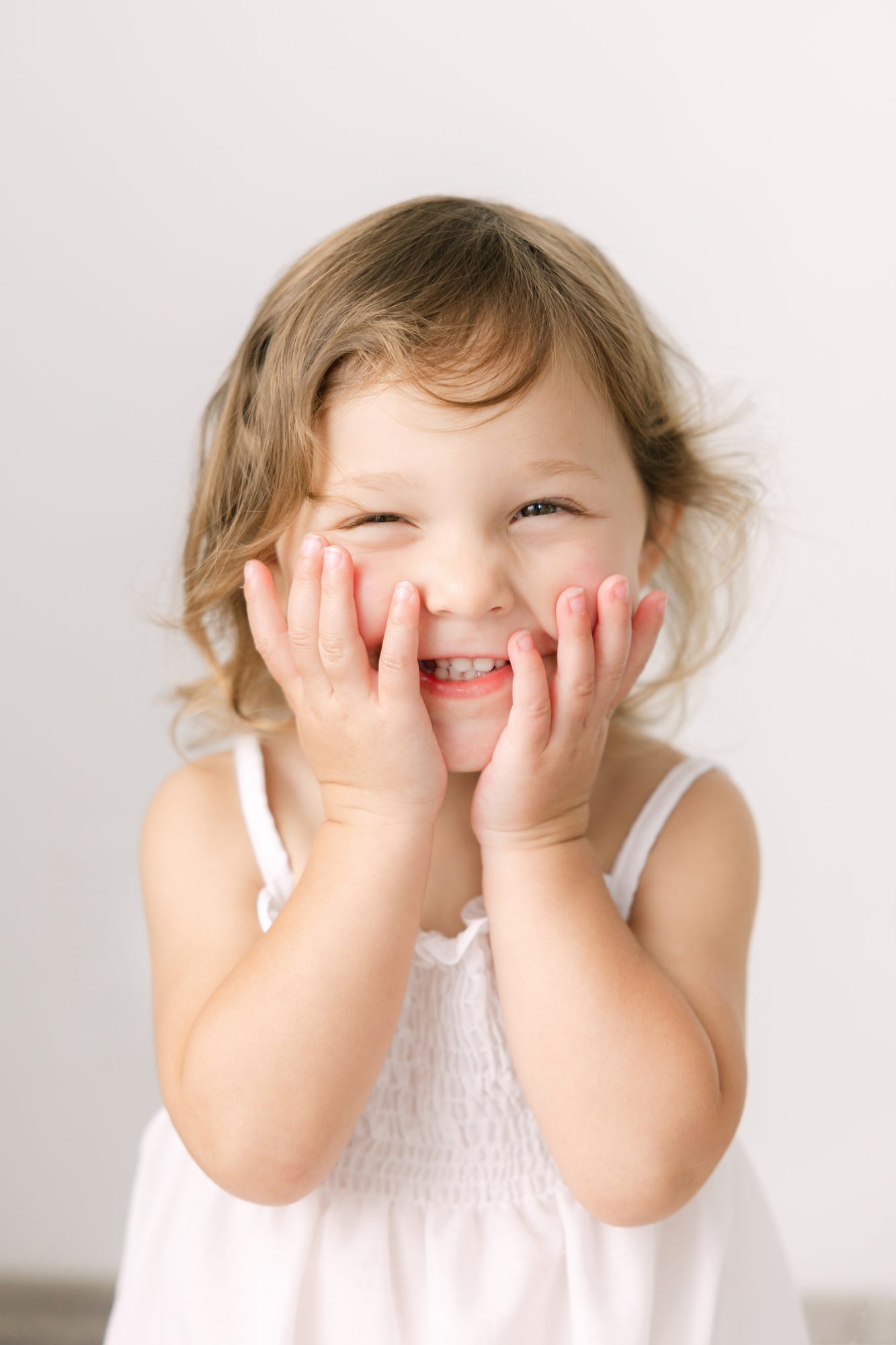 Little girl giggling with her hands on her cheeks, studio portrait