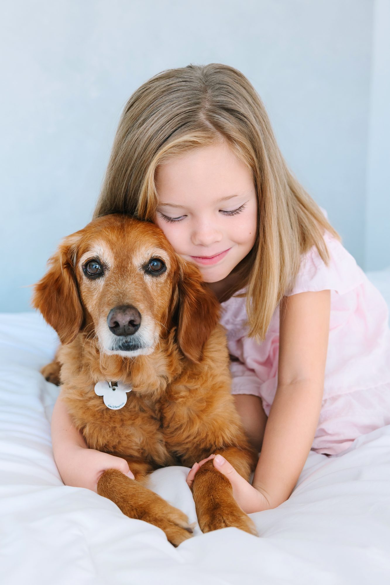 Girl hugging her dog on a white bed during a studio session
