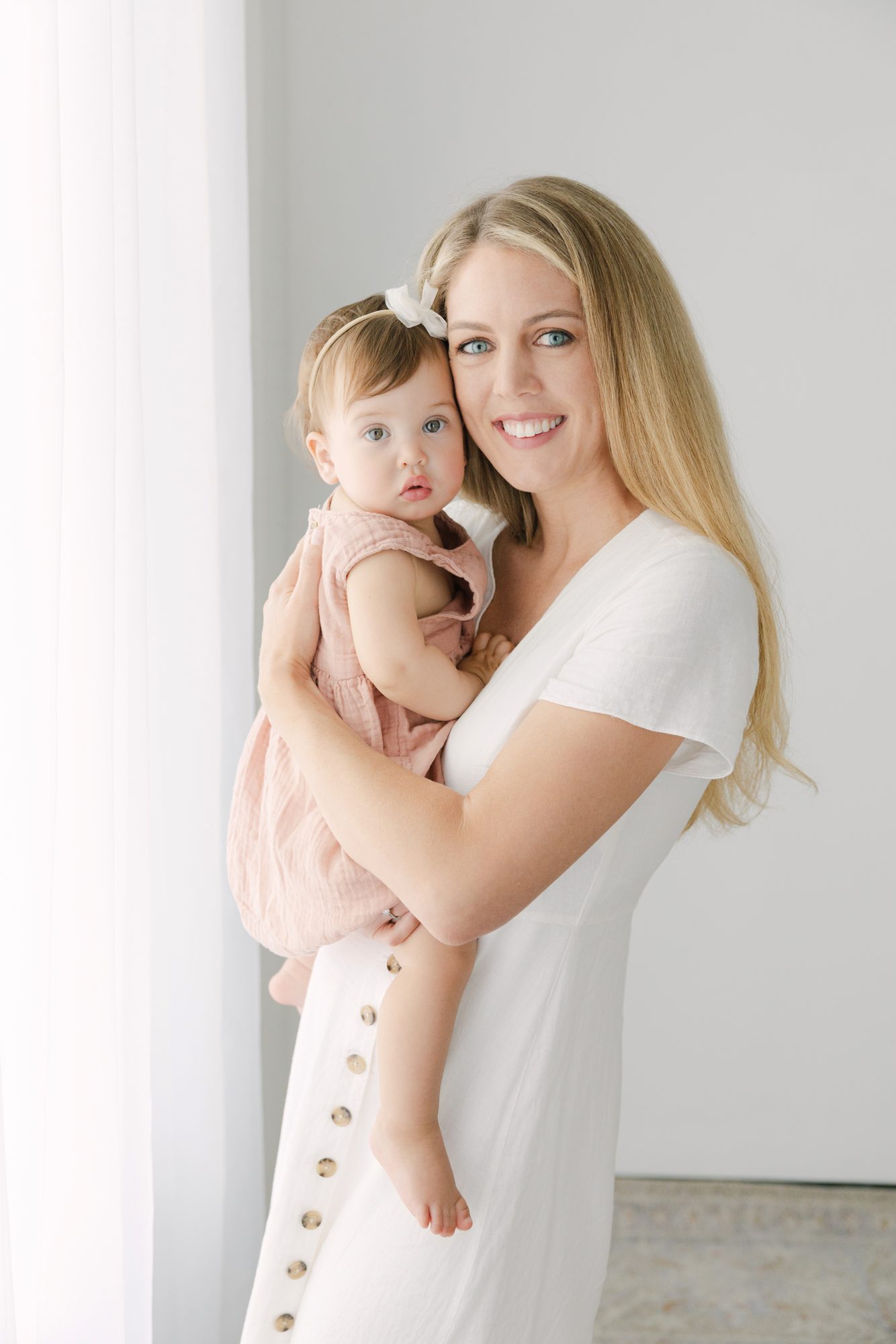 Mother holding her baby daughter beside the window curtains in the Carlsbad studio