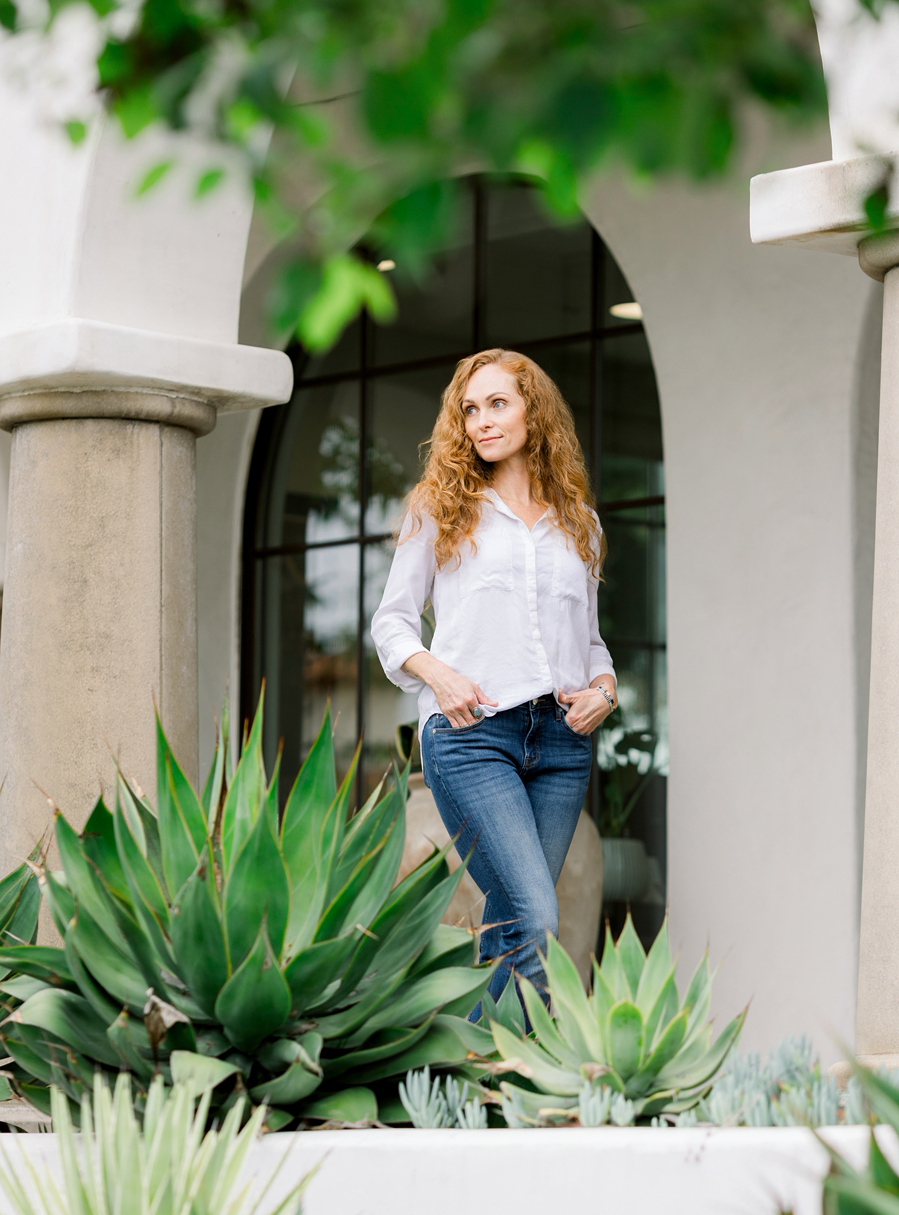 Heather Moreau of Vallentyne photography outside a building with arches, surrounded by lush green succulents.