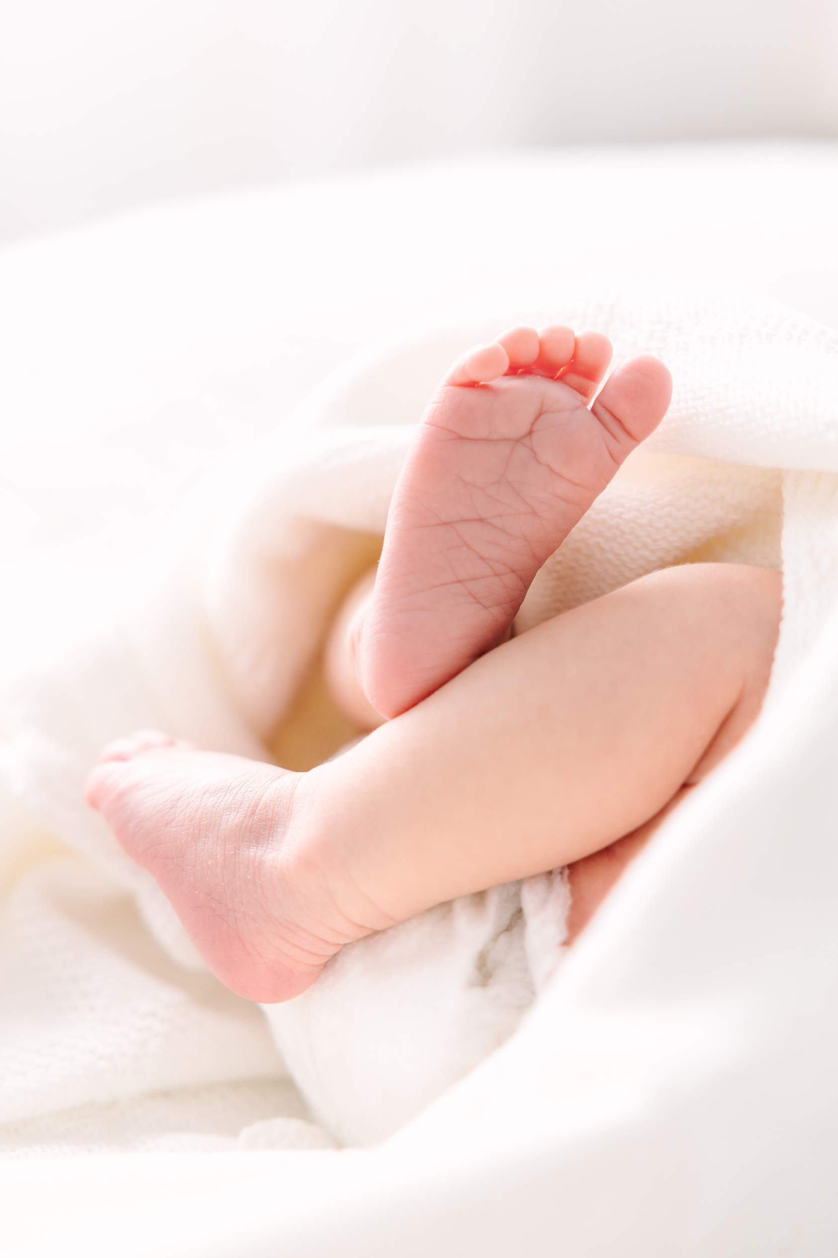 Close-up of a babys feet crossed and resting on a soft white blanket.